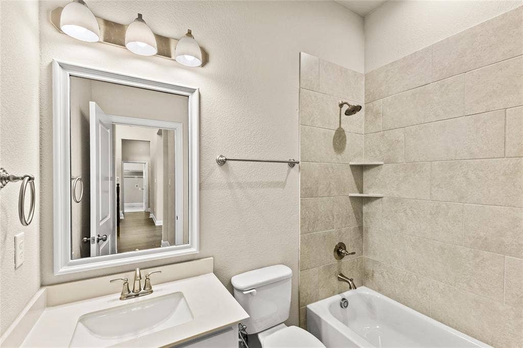 408 Abbott Lane, Waxahachie, TX 75165 Bathroom featuring a vanity with a white countertop and drop-in basin, three-light fixture, framed mirror, and a tub-shower combination with floor-to-ceiling neutral tile surround and integrated shelving