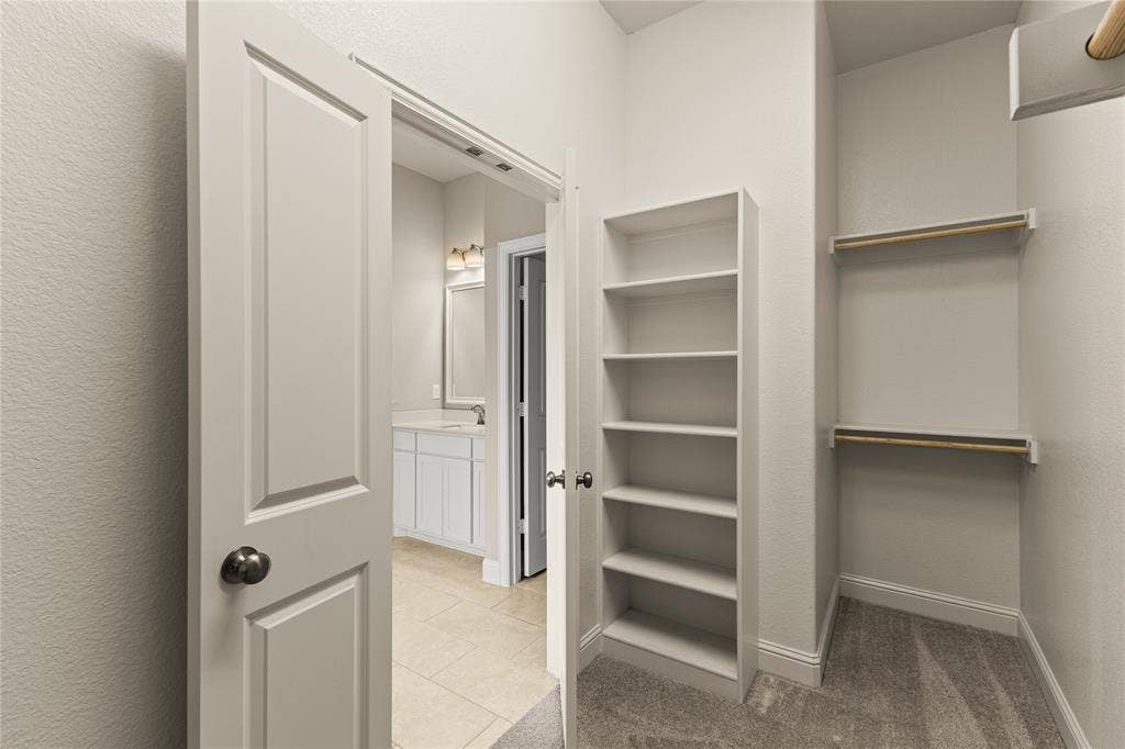 408 Abbott Lane, Waxahachie, TX 75165 Walk-in storage space featuring built-in shelving, dual-tier clothes rods, and carpeted flooring