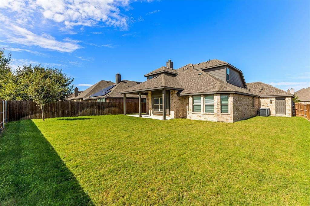 408 Abbott Lane, Waxahachie, TX 75165 Brick and horizontal siding exterior featuring a covered patio, expansive lawn, and wood-panel perimeter fencing