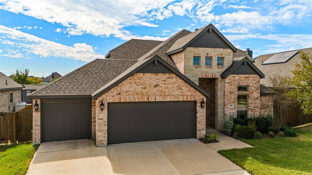 408 Abbott Lane, Waxahachie, TX 75165 Multi-level exterior featuring a brick and stone facade, dual-bay garage, steep-pitched roofline with shingles, and decorative shingle siding accents