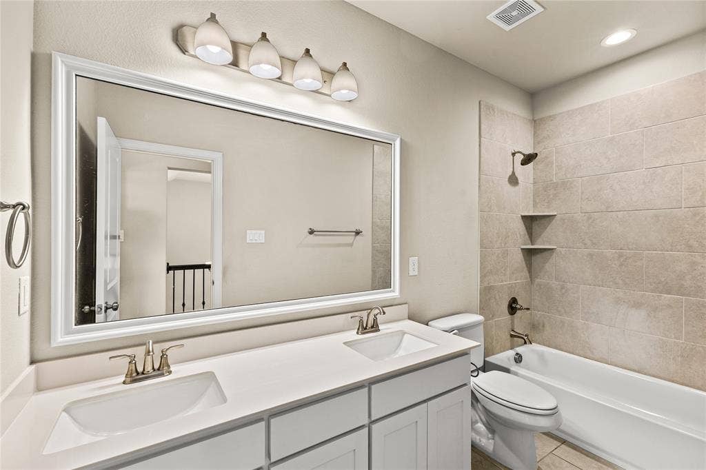 408 Abbott Lane, Waxahachie, TX 75165 Dual-sink vanity with white cabinetry, rectangular under-mount sinks, large wall-mounted mirror, and tile-surround shower and tub combination