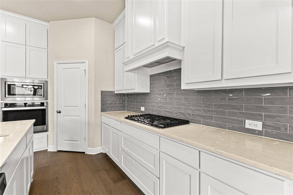 408 Abbott Lane, Waxahachie, TX 75165 Kitchen featuring white shaker-style cabinetry, a gray subway tile backsplash, light-toned solid surface countertops, built-in stainless steel double wall ovens, and wood-finish flooring