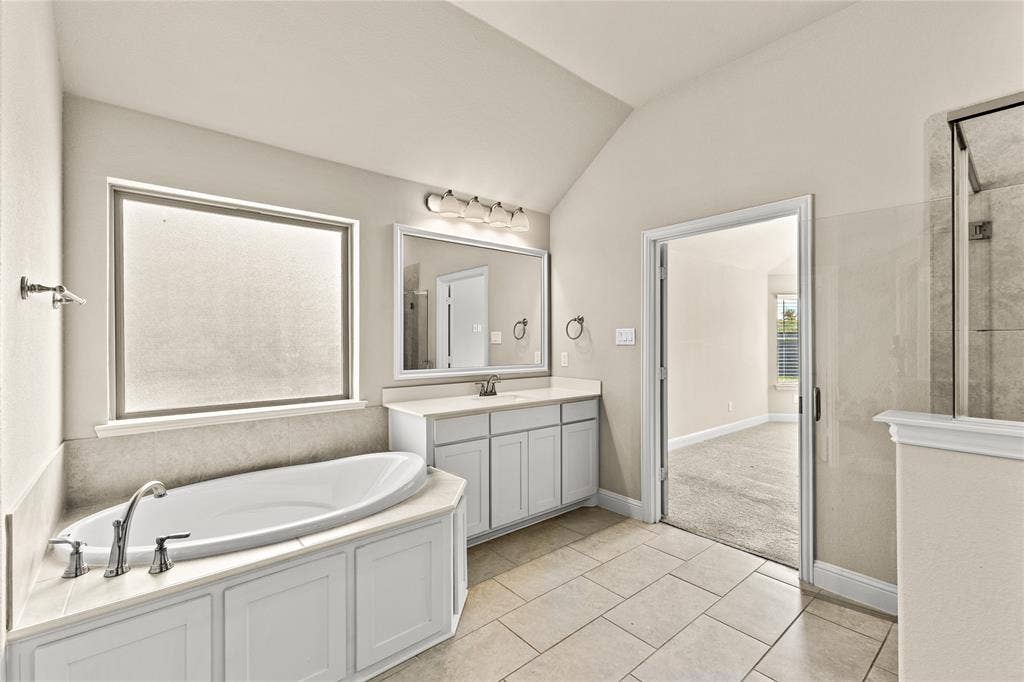 408 Abbott Lane, Waxahachie, TX 75165 Built-in soaking tub with a tiled surround, dual-sink vanity with white cabinetry, framed vanity mirror, glass-enclosed shower, and neutral tile flooring