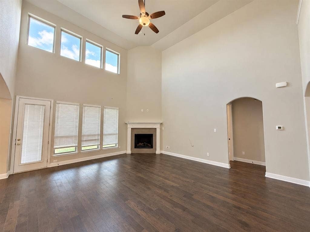 6414 Waggoner Court, Temple, TX 76502 Expansive living area featuring vaulted ceilings, wood-finish flooring, a corner fireplace with a neutral surround, floor-to-ceiling windows, and a ceiling fan