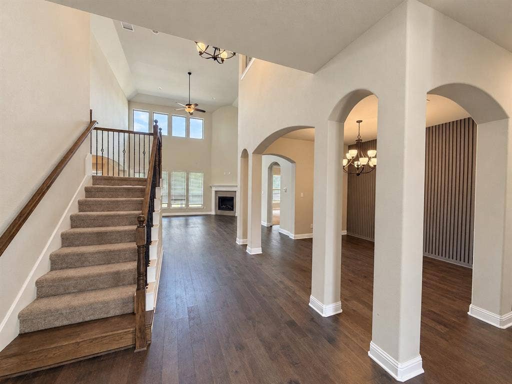 6414 Waggoner Court, Temple, TX 76502 Interior area featuring soaring ceilings, a central staircase with a dark wood-finish railing, dark hardwood flooring, architectural arched openings, and decorative vertical-slat wall paneling