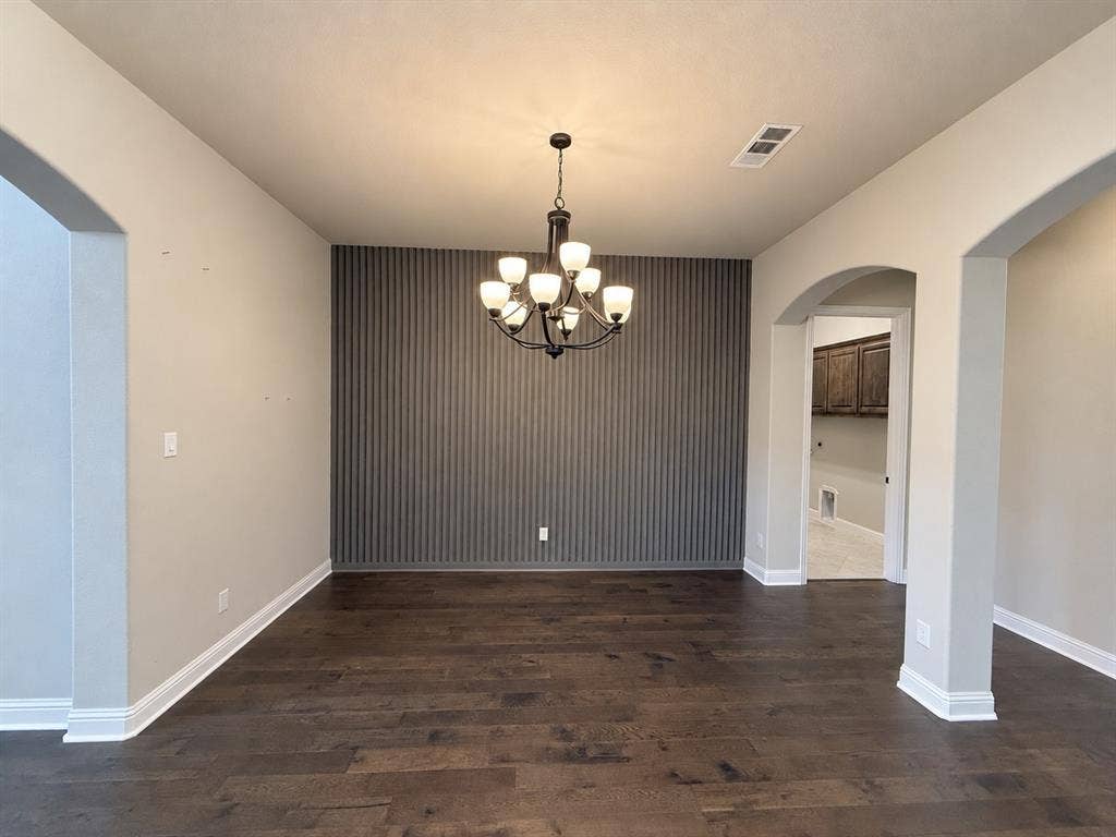 6414 Waggoner Court, Temple, TX 76502 Hardwood flooring, vertical slat accent wall, and multi-arm chandelier featuring frosted glass shades, framed by architectural archways