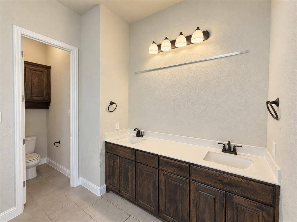 6414 Waggoner Court, Temple, TX 76502 Dual-sink vanity with dark-finish cabinetry, light-toned countertop, oil-rubbed bronze fixtures, and four-light vanity fixture