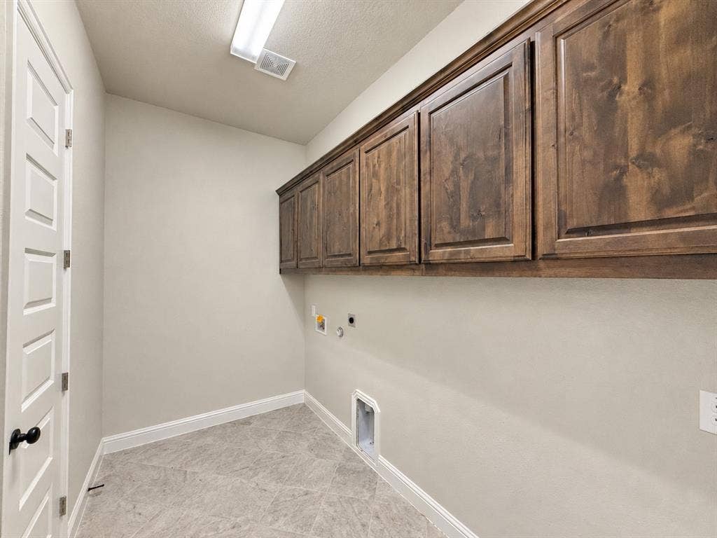 6414 Waggoner Court, Temple, TX 76502 Utility area featuring stained wood cabinetry, grey tile flooring, and a five-panel interior door with matte black hardware