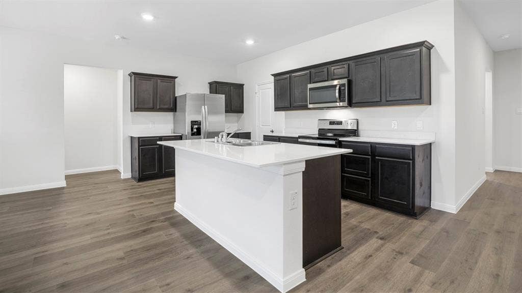320 Ridan Drive, Waxahachie, TX 75165 Kitchen featuring an expansive island with a white countertop, dark wood-finish cabinetry, stainless steel appliances, white subway tile backsplash, and wood-finish flooring