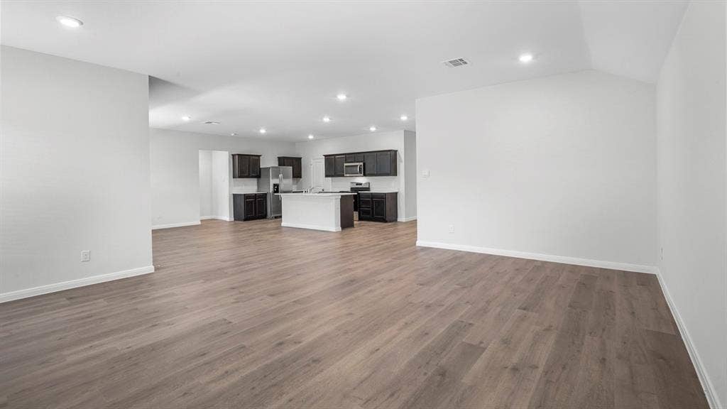 320 Ridan Drive, Waxahachie, TX 75165 Open-concept living space featuring wood-finish flooring, recessed lighting, and a kitchen with dark cabinetry, light countertops, and a central island