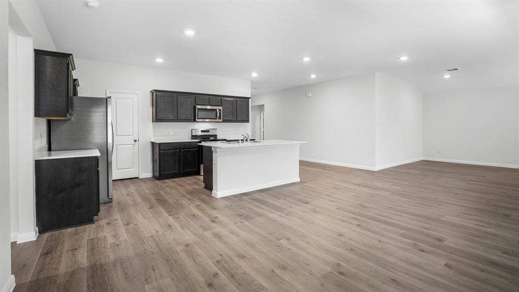 320 Ridan Drive, Waxahachie, TX 75165 Open-concept living area featuring wood-finish flooring, recessed lighting, and a kitchen island with a double basin sink