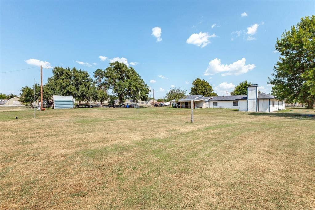 7400 County Road 131A, Terrell, TX 75161 Expansive grass lot featuring mature trees, a detached metal storage structure, and a masonry exterior chimney