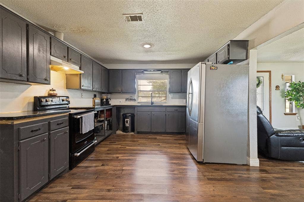 7400 County Road 131A, Terrell, TX 75161 Kitchen featuring dark-finish cabinetry, stainless steel refrigerator, black electric range, wood-finish flooring, and natural light from a window over the sink