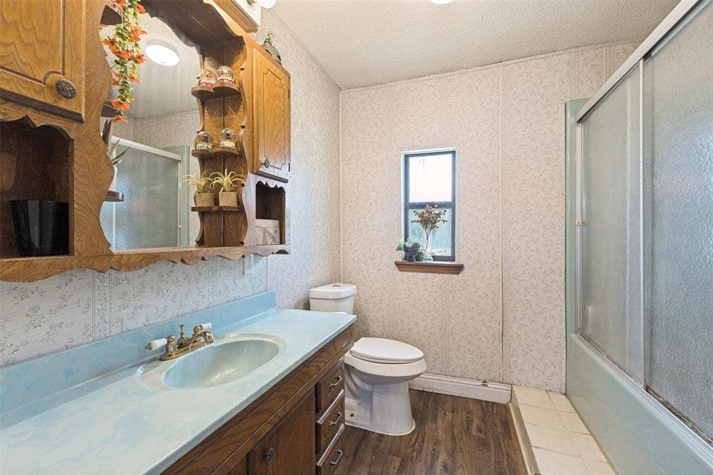 7400 County Road 131A, Terrell, TX 75161 Wood-finish cabinetry featuring built-in shelving, integrated basin with metal hardware, tub and shower combination with sliding glass doors, and wood-finish flooring