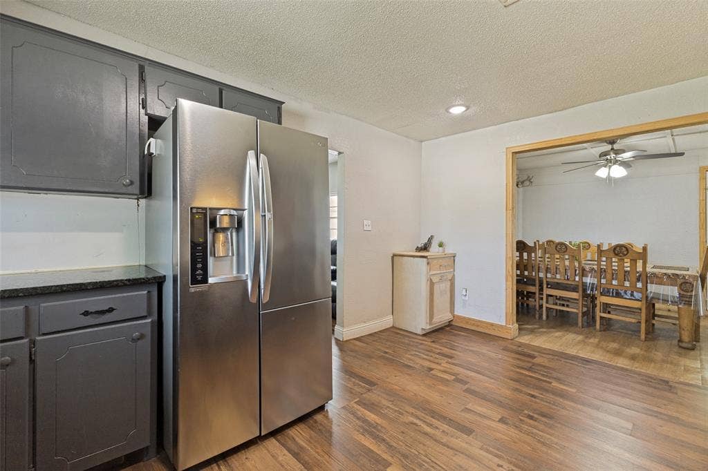 7400 County Road 131A, Terrell, TX 75161 Kitchen featuring charcoal-toned cabinetry, stone-surface countertops, and a stainless-steel refrigerator, with wood-finish flooring extending into the surrounding area