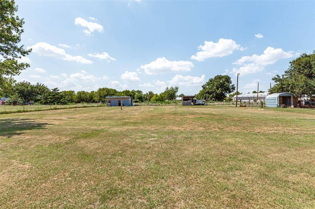 7400 County Road 131A, Terrell, TX 75161 Expansive open lot featuring grass landscape, metal storage outbuildings, and wire perimeter fencing