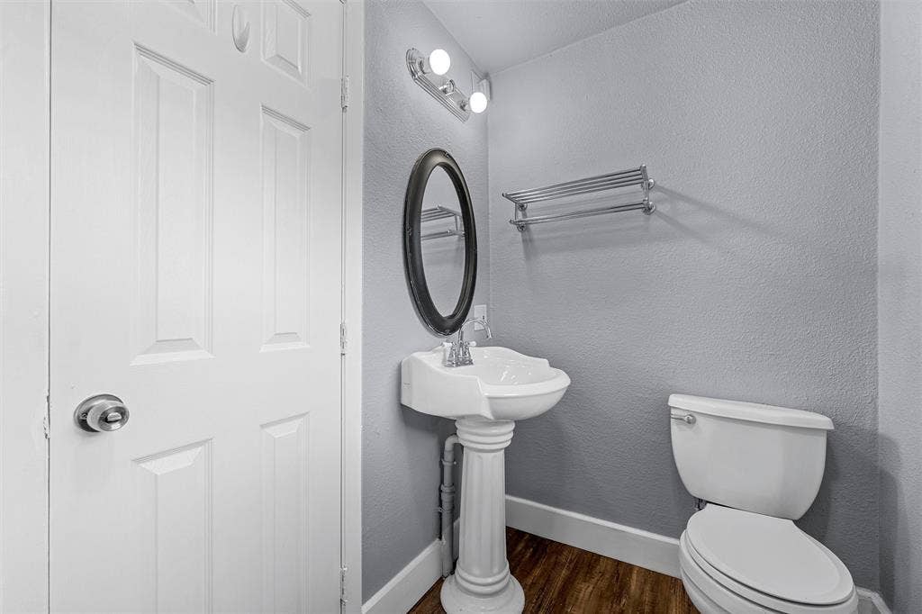 2222 Speight Avenue, Waco, TX 76706 White pedestal sink with chrome faucet, oval wall-mounted mirror, metal wall-mounted towel rack, and wood-finish flooring