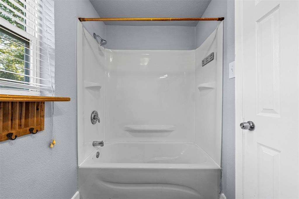 2222 Speight Avenue, Waco, TX 76706 Full-height acrylic tub surround with integrated shelving, chrome shower hardware, window with horizontal blinds, and a built-in wooden wall-mounted organizer