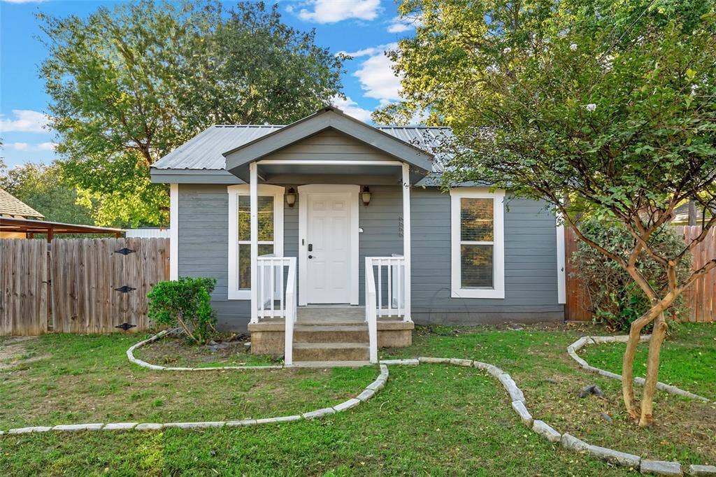 2222 Speight Avenue, Waco, TX 76706 Exterior featuring grey horizontal lap siding, a metal roof, a covered front porch with white railings, and decorative stone garden edging