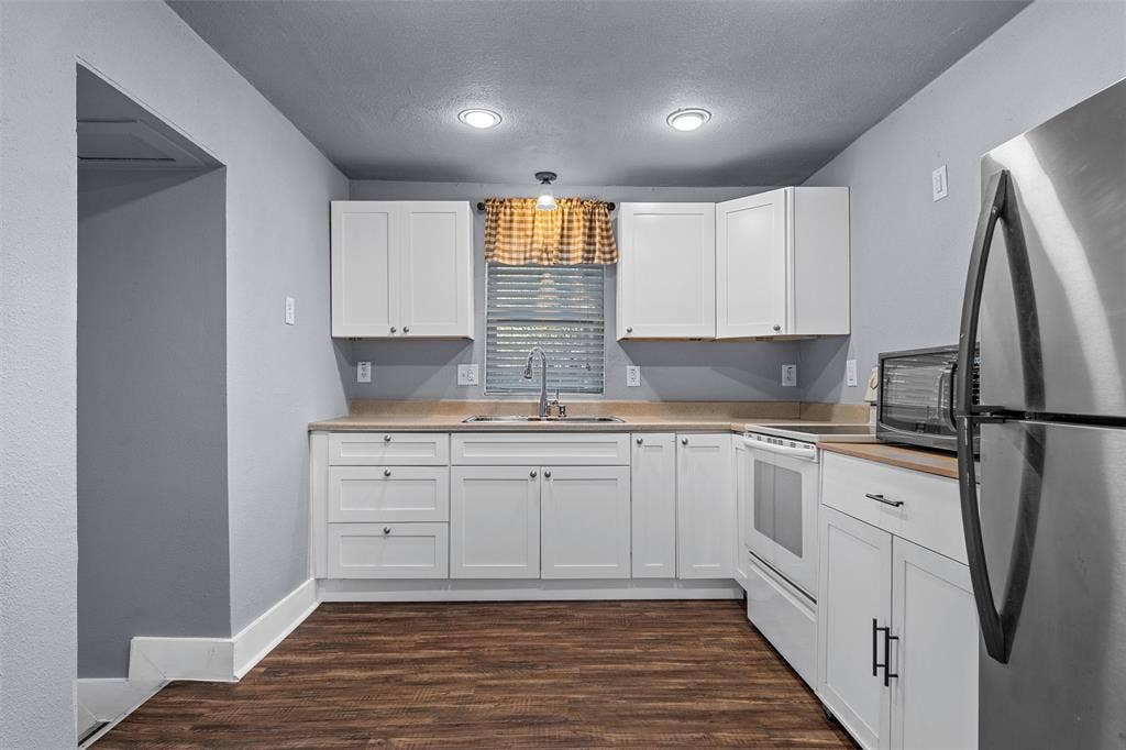2222 Speight Avenue, Waco, TX 76706 Kitchen featuring white shaker-style cabinetry, solid-surface countertops, recessed lighting, stainless steel refrigerator, and wood-finish flooring