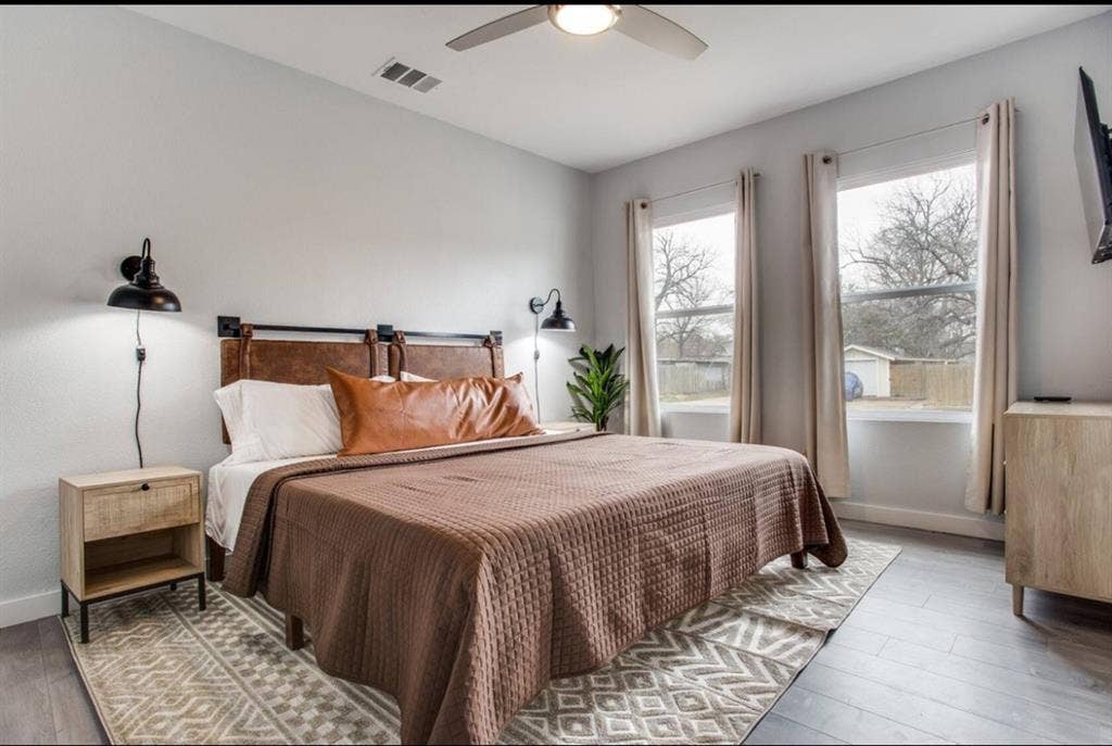 1606 W 12th Street, Dallas, TX 75208 Wood-finish flooring, dual wall-mounted matte black light fixtures, ceiling fan with integrated light, and large windows with natural light