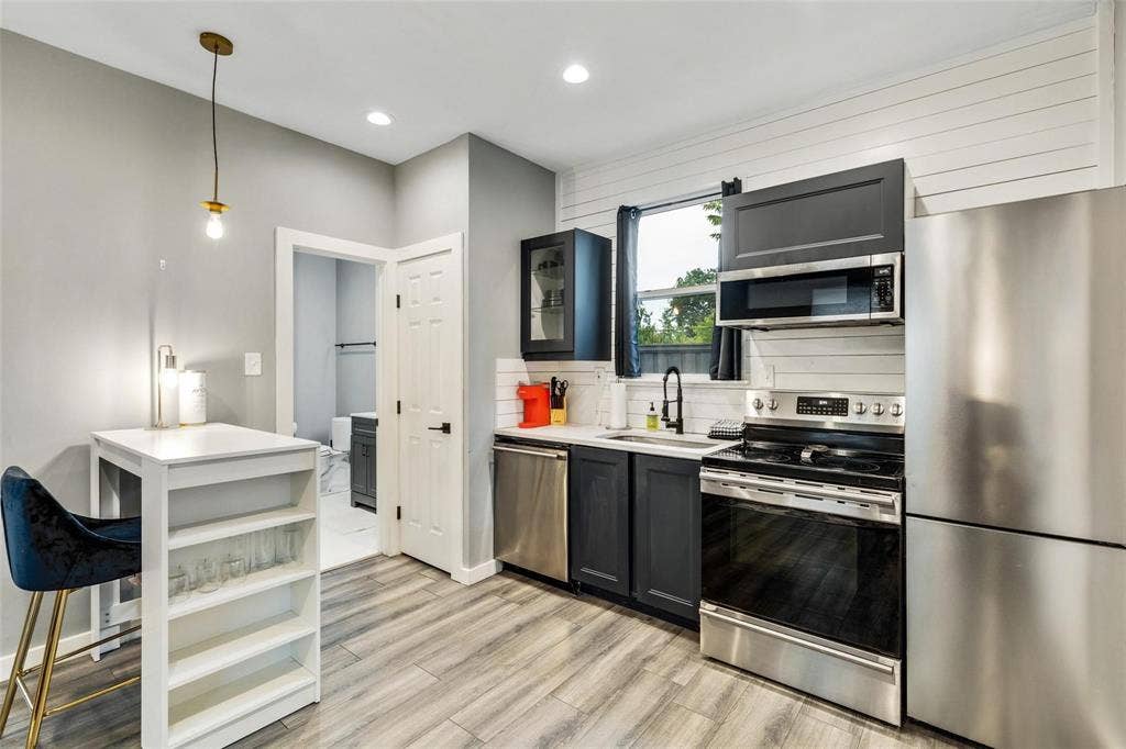 1606 W 12th Street, Dallas, TX 75208 Kitchen featuring dark-finish cabinetry, stainless steel appliances, wood-finish flooring, horizontal wall paneling, and recessed lighting