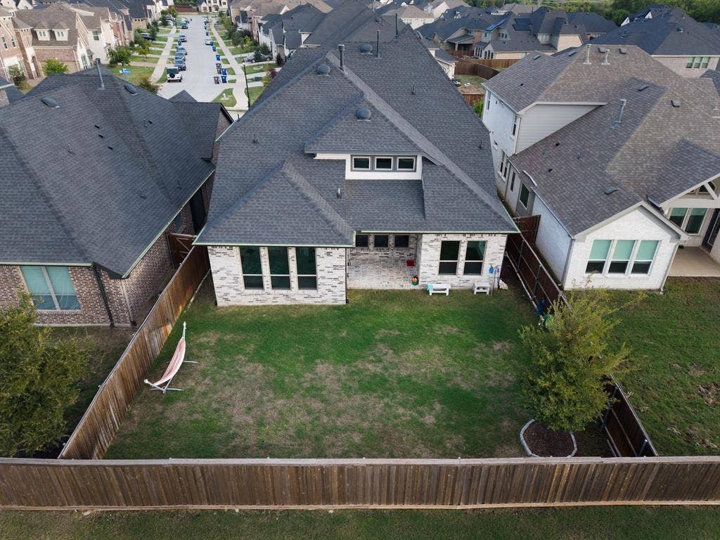 415 Rock Rose Lane, Wylie, TX 75098 Aerial perspective of a multi-gabled residence featuring a light-toned brick facade, asphalt shingle roofing, a covered patio area, and a fully fenced backyard