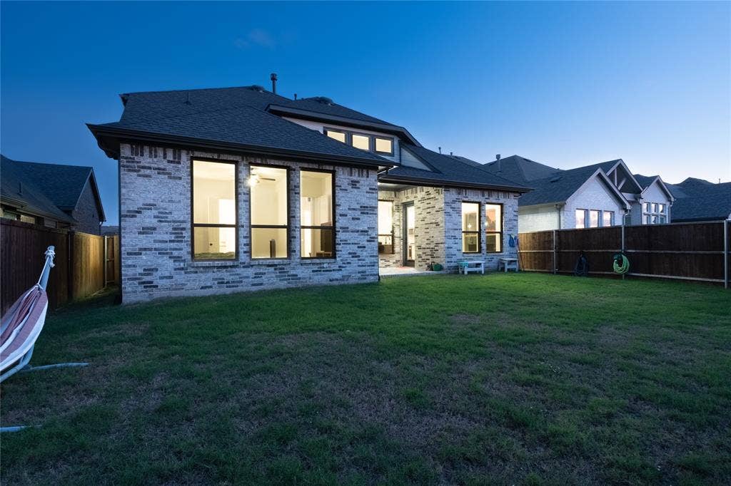 415 Rock Rose Lane, Wylie, TX 75098 Rear elevation featuring brick masonry, large multi-pane windows, a covered patio, and wood privacy fencing surrounding the lawn
