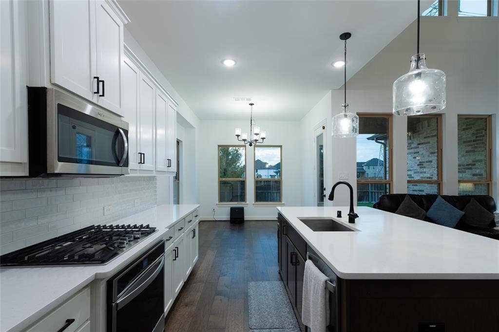 415 Rock Rose Lane, Wylie, TX 75098 Kitchen featuring white shaker-style cabinetry, quartz countertops, a central island with a matte black faucet, stainless steel appliances, and wood-finish flooring