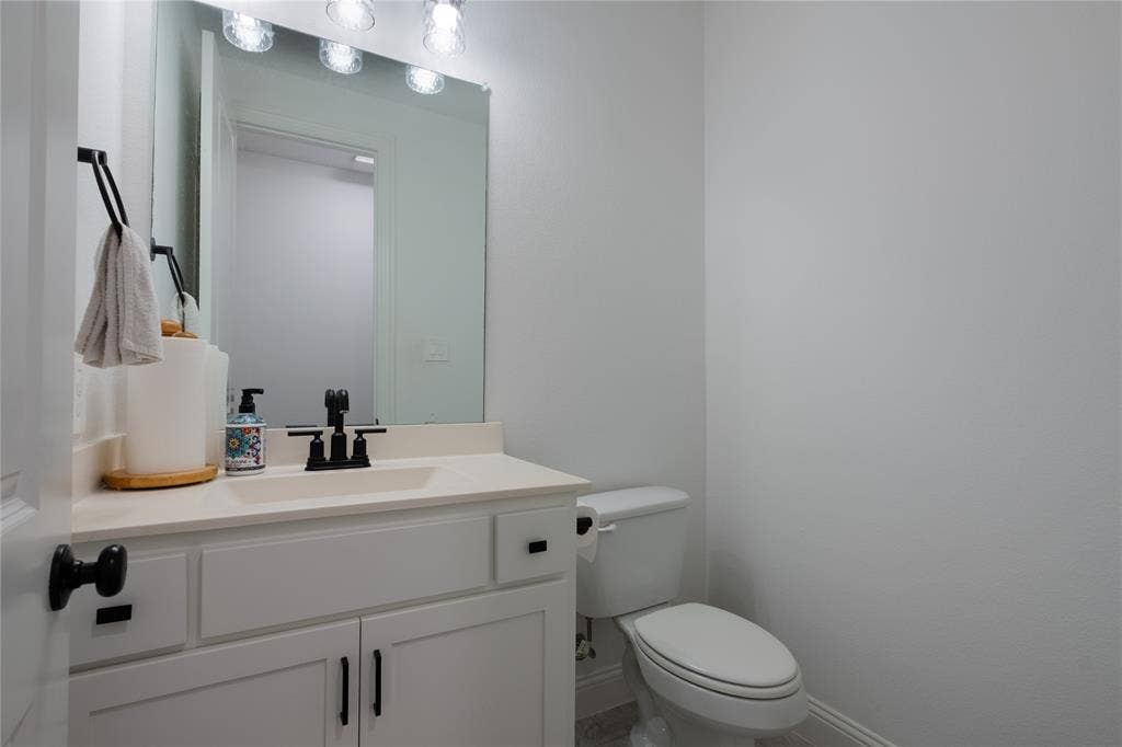 415 Rock Rose Lane, Wylie, TX 75098 White vanity cabinet featuring a solid-surface countertop, rectangular integrated sink, matte black faucet, and matching cabinet hardware, paired with a large wall-mounted mirror and integrated vanity lighting