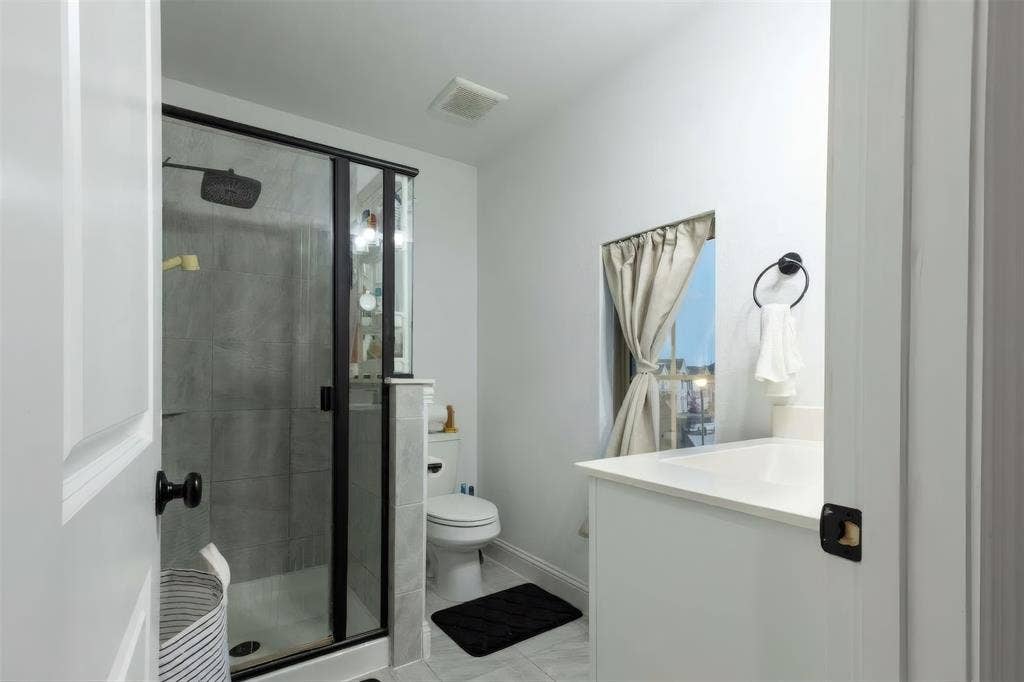 415 Rock Rose Lane, Wylie, TX 75098 Bathroom featuring a glass-enclosed shower with dark-toned hardware, white cabinetry, rectangular under-mount sink, and neutral tile flooring