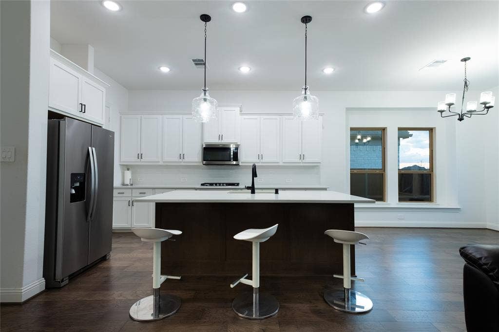 415 Rock Rose Lane, Wylie, TX 75098 Kitchen featuring white shaker-style cabinetry, central island with a solid surface countertop, stainless steel refrigerator, dark wood-finish flooring, and recessed ceiling lighting