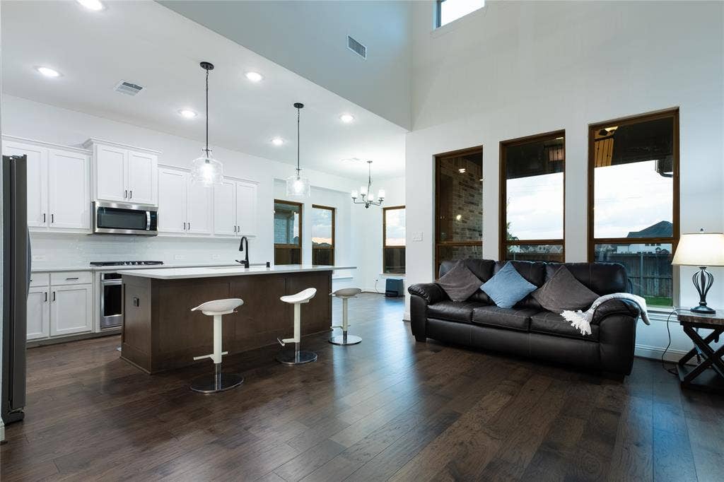 415 Rock Rose Lane, Wylie, TX 75098 Open-concept living space featuring high ceilings, wood-finish flooring, white cabinetry, a kitchen island with a stone-finish countertop, and large windows