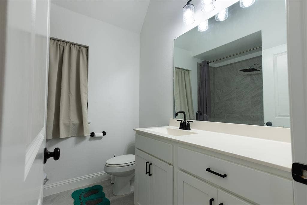 415 Rock Rose Lane, Wylie, TX 75098 Bathroom featuring a white vanity with matte black hardware, a solid-surface countertop with an integrated sink, a large wall-mounted mirror, and a multi-bulb vanity light fixture