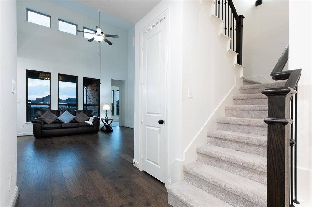 415 Rock Rose Lane, Wylie, TX 75098 Vaulted ceilings, wood-finish flooring, staircase with carpeted treads and dark-stained wood railings, and oversized vertical windows