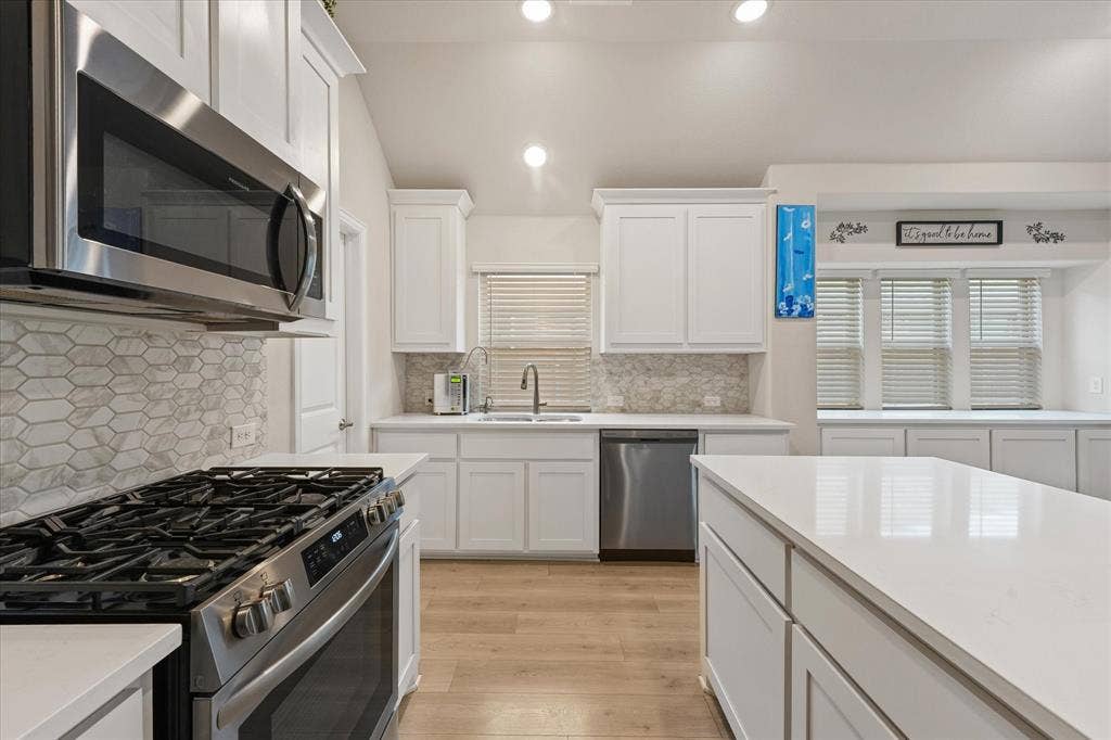 1958 Snowball Lane, Glenn Heights, TX 75154 Kitchen featuring white shaker cabinetry, a central island with a quartz countertop, stainless steel appliances, and a hexagon-patterned stone backsplash