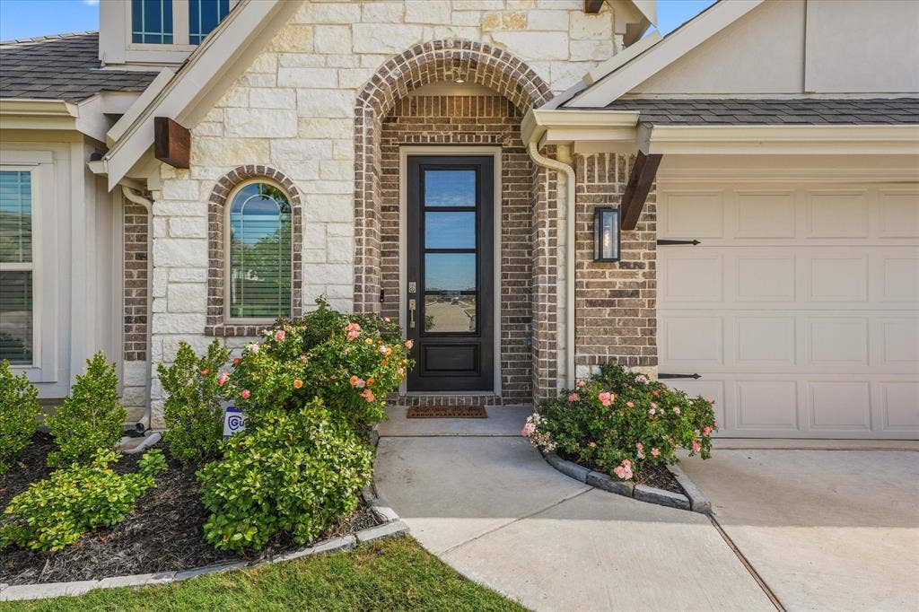 1958 Snowball Lane, Glenn Heights, TX 75154 Exterior facade featuring stone and brick masonry, an arched entryway with a multi-pane glass door, and a concrete walkway