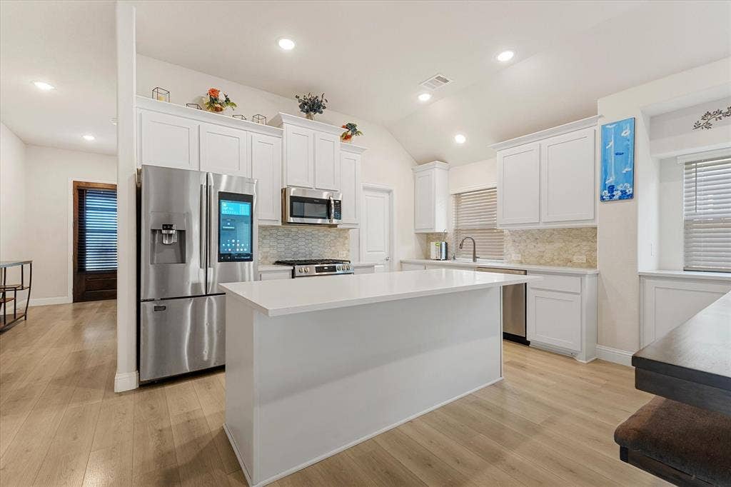 1958 Snowball Lane, Glenn Heights, TX 75154 Kitchen featuring white shaker-style cabinetry, a central island with a solid surface countertop, stainless steel appliances, wood-finish flooring, and recessed lighting