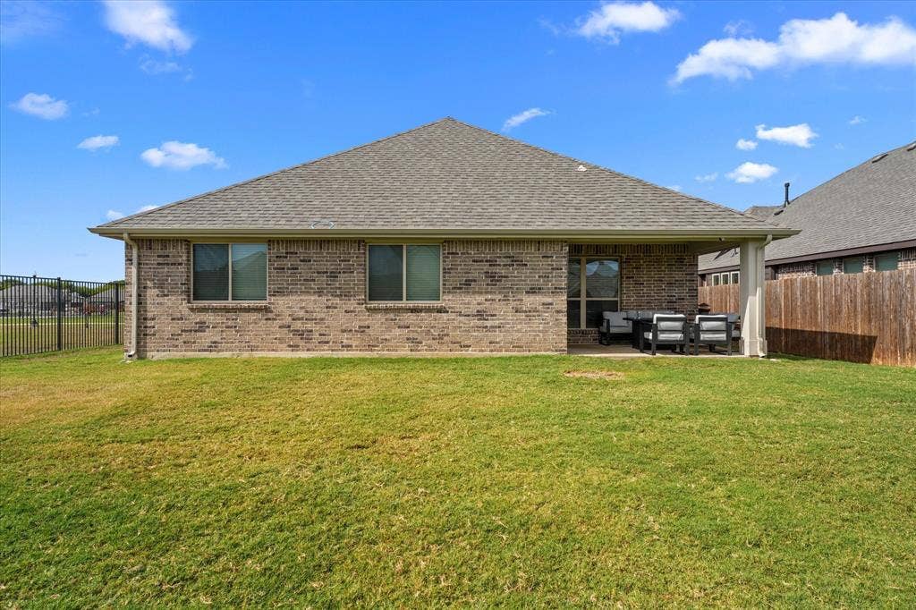 1958 Snowball Lane, Glenn Heights, TX 75154 Rear brick exterior featuring a covered patio, a grass lawn, and wood-slat fencing