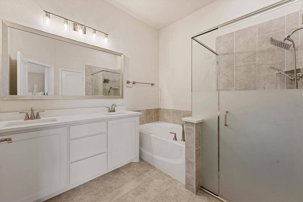 1958 Snowball Lane, Glenn Heights, TX 75154 Bathroom featuring a dual-sink vanity with white cabinetry, a full-width vanity mirror, a separate soaking tub, and a walk-in shower with tile surround and frosted glass door