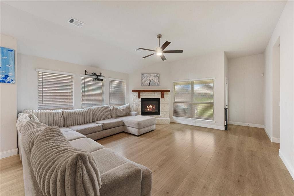 1958 Snowball Lane, Glenn Heights, TX 75154 Living area featuring wood-finish flooring, vaulted ceilings, a stone-surround fireplace with a timber mantel, and an integrated ceiling fan