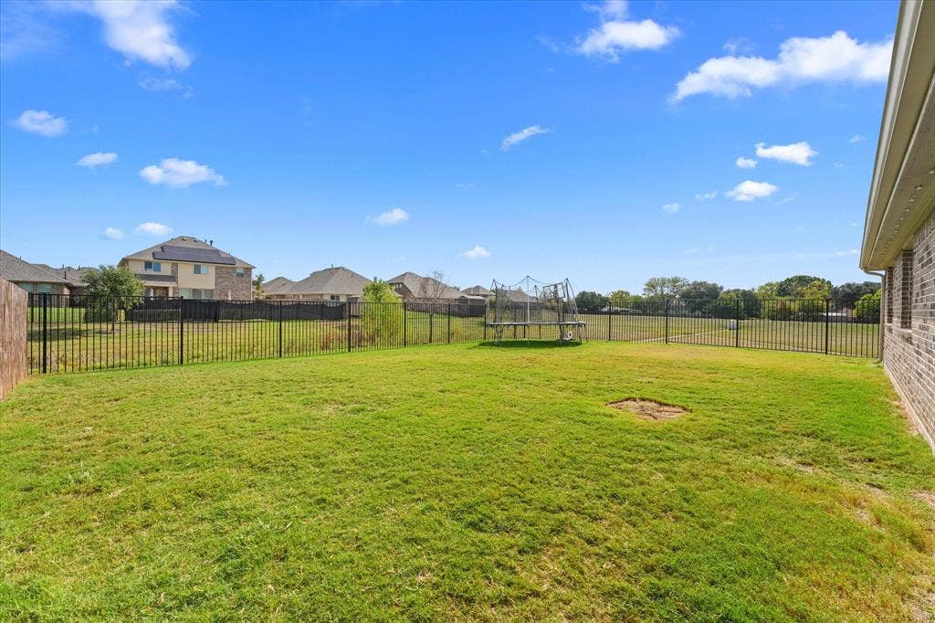 1958 Snowball Lane, Glenn Heights, TX 75154 Expansive backyard featuring a large grass lawn, perimeter black metal fencing, and brick exterior siding