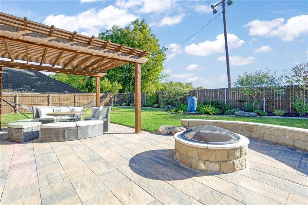 401 Mesa, Lone Oak, TX 75453 Backyard featuring a paved stone patio, a wooden pergola, a circular stone fire pit with a masonry seating wall, and a wood privacy fence