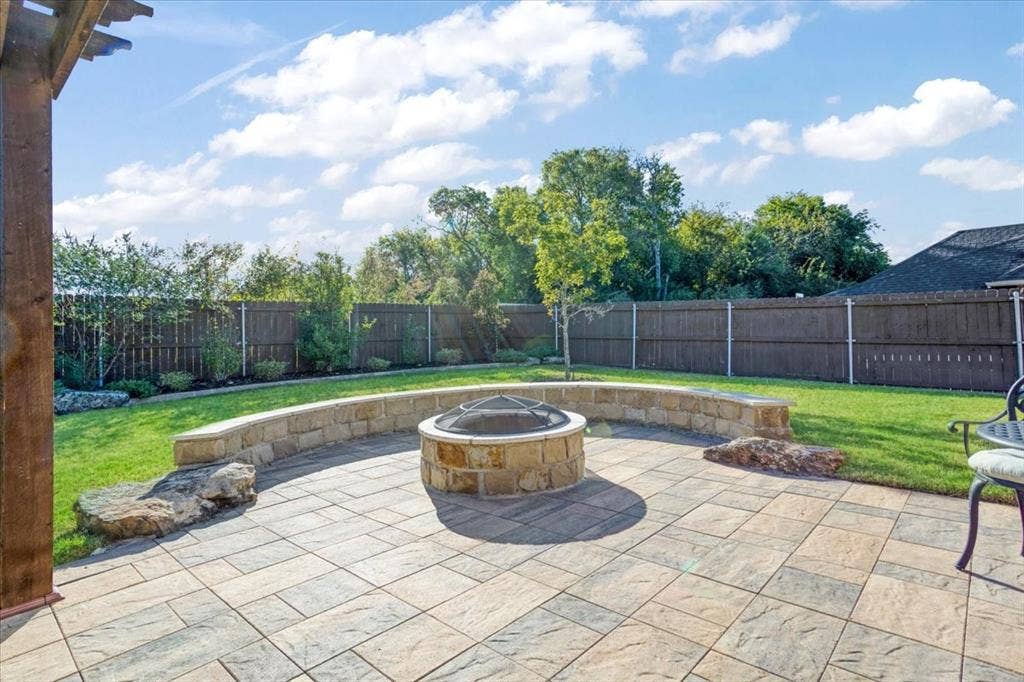 401 Mesa, Lone Oak, TX 75453 Backyard featuring a paved stone patio, built-in natural stone fire pit, curved stone seating wall, and wood privacy fencing