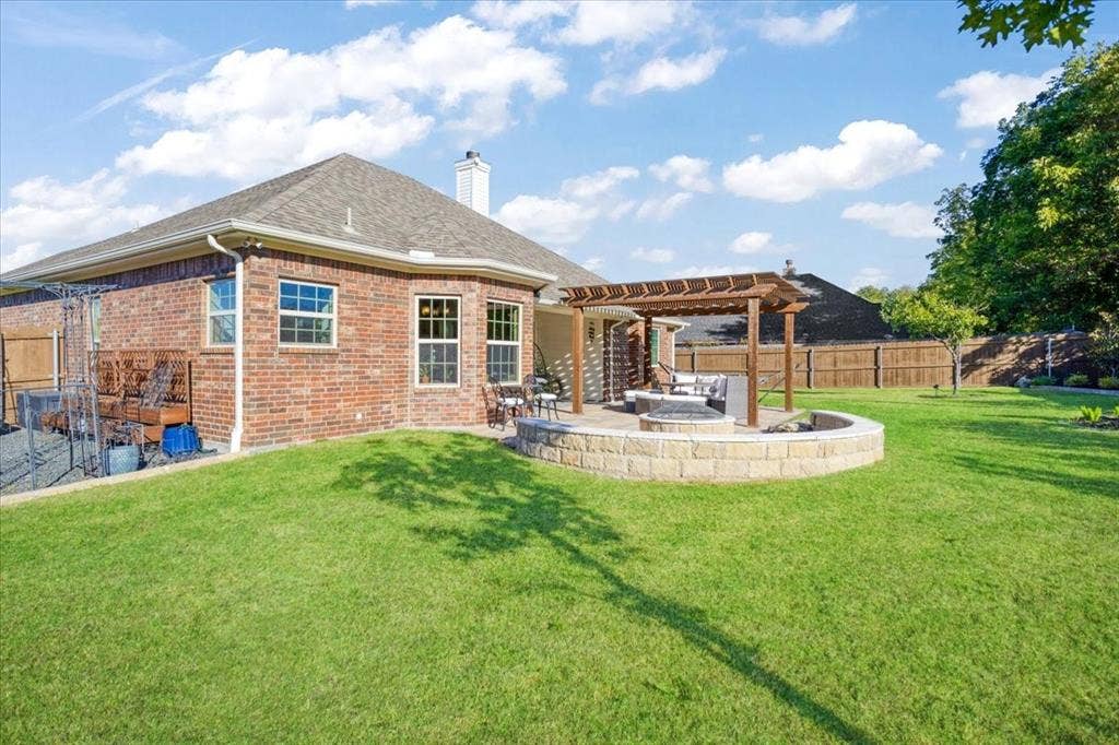 401 Mesa, Lone Oak, TX 75453 Brick exterior residence featuring a covered pergola, stone-accented fire pit, paved patio, and fenced backyard