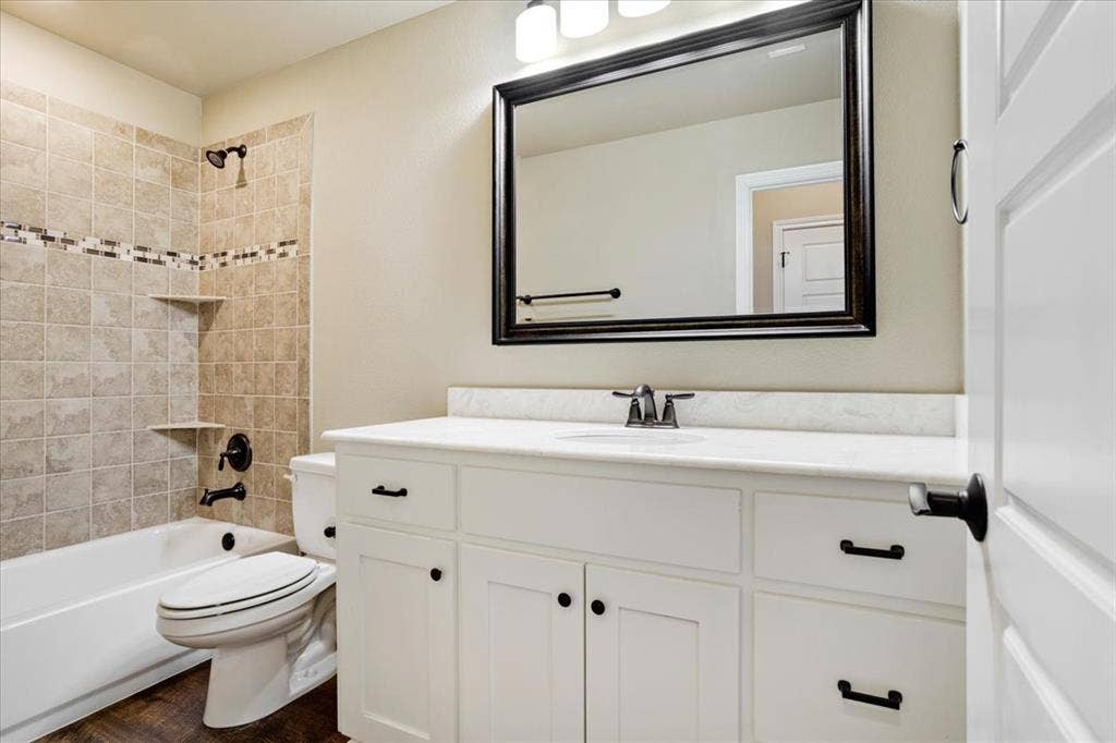 401 Mesa, Lone Oak, TX 75453 White vanity cabinet with quartz countertop, undermount sink, and matte black hardware, paired with a shower-tub combination featuring tiled walls with a decorative accent border and matte black fixtures