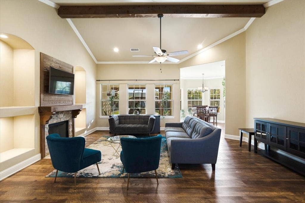 401 Mesa, Lone Oak, TX 75453 Living room featuring vaulted ceilings, a central exposed wood beam, wood-finish flooring, a stone-surround fireplace with a wooden mantel, and built-in recessed shelving