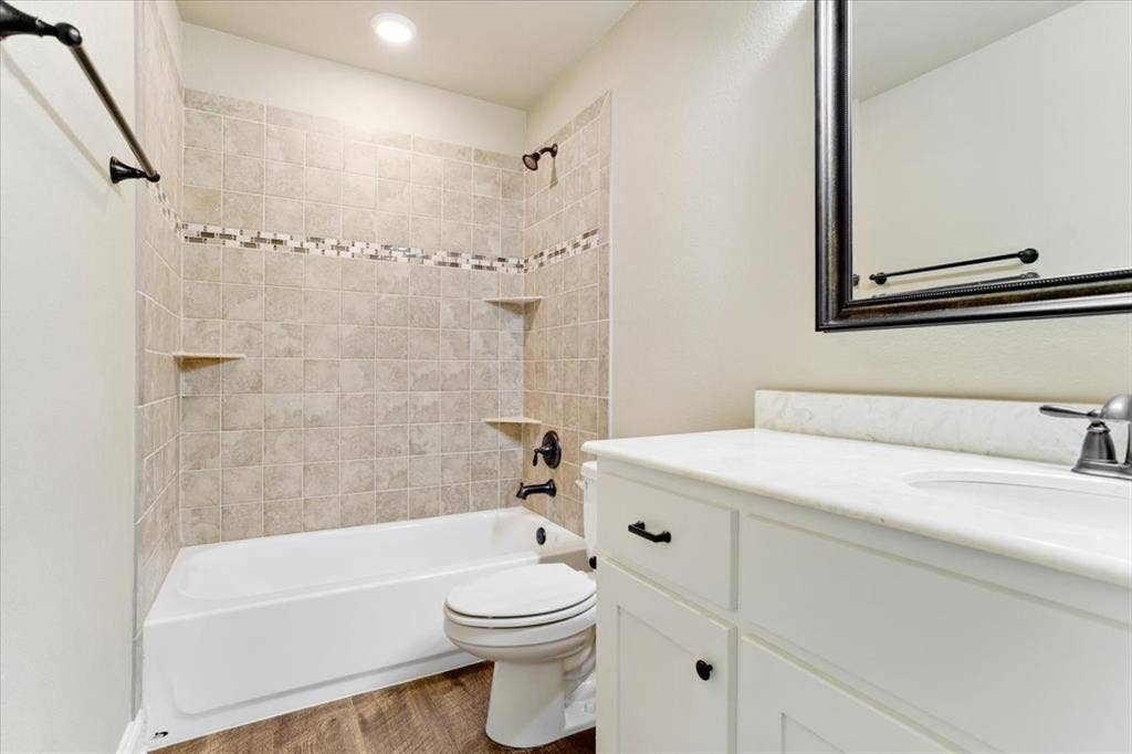 401 Mesa, Lone Oak, TX 75453 White vanity with stone-finish countertop, undermount sink, oil-rubbed bronze hardware, tub-shower combination with decorative tile inlay, and wood-finish flooring