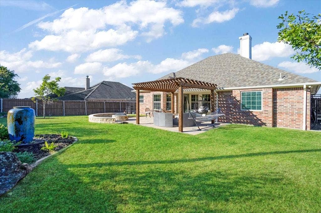 401 Mesa, Lone Oak, TX 75453 Brick exterior residence featuring a wooden pergola, concrete patio, stone fire pit, and expansive lawn