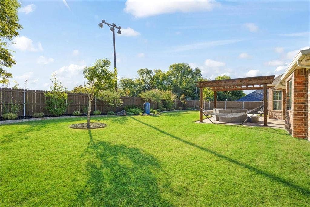 401 Mesa, Lone Oak, TX 75453 Expansive backyard featuring a wood-beam pergola, brick exterior siding, manicured lawn, and perimeter wood fencing